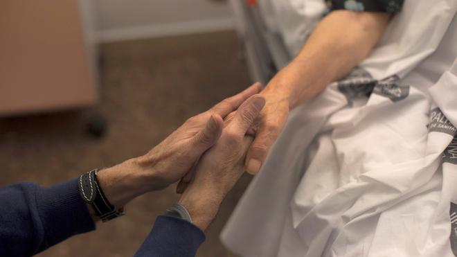 María es acariciada por las manos de su marido José, minutos antes de que ella culmine el proceso para morir por eutanasia. / BIEL ALIÑO / EFE