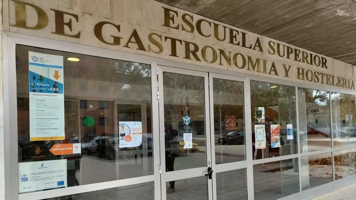 Sede del CES Juan Pablo II y Escuela de Gastronomía del Polígono de Toledo. Mantiene en el rótulo de arriba su anterior denominación como "Escuela Superior de Gastronomía" aunque en la puerta central ya aparece el logo de Educatio Servanda. elDiarioclm.es