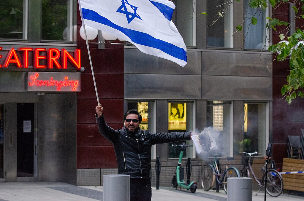 Salwan Momika alza una bandera de Israel mientras quema un Corán en 2023